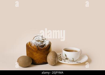 A traditional Easter cake sprinkled with powdered sugar, colored beige eggs and a cup of black tea in a white mug and a sprig of apple blossom. Holida Stock Photo