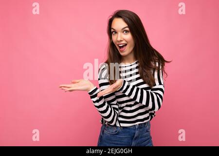 Portrait photo of young happy positive beautiful brunette woman with sincere emotions wearing casual striped pullover isolated on pink background with Stock Photo