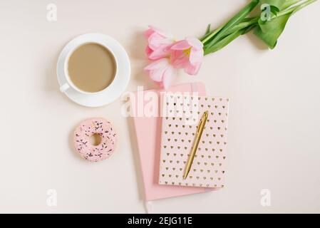 Trendy stylish concept for a female blogger, freelancer: pink diary, notebook, Donat, pink tulips and an cup of coffee  on beige background. Working f Stock Photo