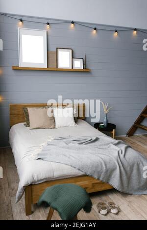 Retro garland of incandescent lamps on the walls of a gray bedroom room in the house. The Scandinavian interior of the bedroom with a double bed and a Stock Photo