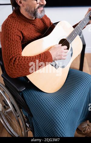 cropped view of smiling disabled man playing acoustic guitar in wheelchair Stock Photo