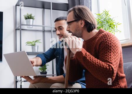 young hispanic man pointing at laptop near father with walking stick Stock Photo