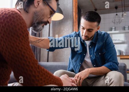 young hispanic man calming sad father at home, blurred foreground Stock Photo