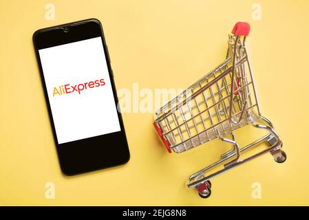 Aliexpress logo on black screen of smartphone with shopping cart on a yellow background Stock Photo