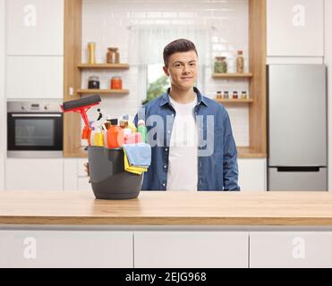 Young man in a kitchen posing with a bucket full of cleaning supplies Stock Photo