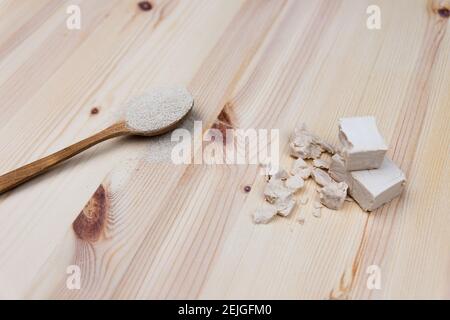 Two different types of yeast on wooden background. Dry yeast in a wooden spoon and fresh bakers yeast in cubes and broken pieces. Baking and making br Stock Photo