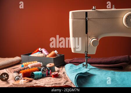 Colored threads, fabrics, and a sewing machine on a brown background. Horizontal orientation with space for copying. The concept of sewing. Stock Photo