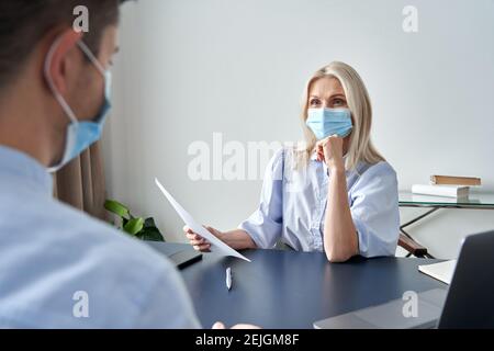 Female hr manager wearing face mask holding cv at job interview. Stock Photo