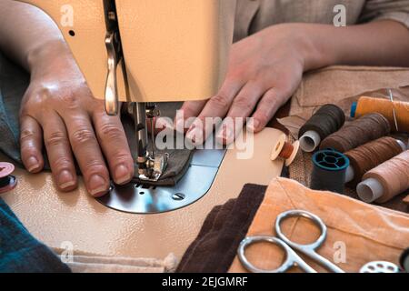 Women's hands sew on a sewing machine against the background of fabrics and threads. Horizontal orientation. Stock Photo
