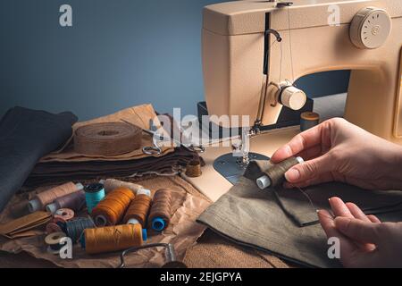 Tailor's hands, thread, fabric and sewing machine on a blue background. Side view with copy space. Stock Photo