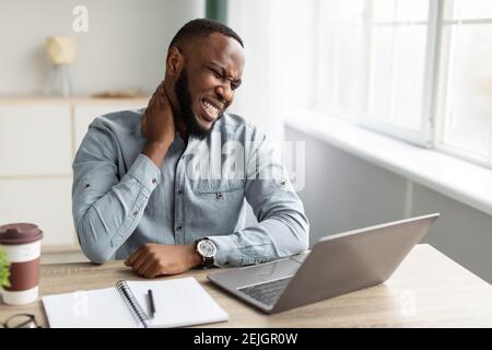 Black Man Massaging Aching Neck Suffering From Pain At Workplace Stock Photo