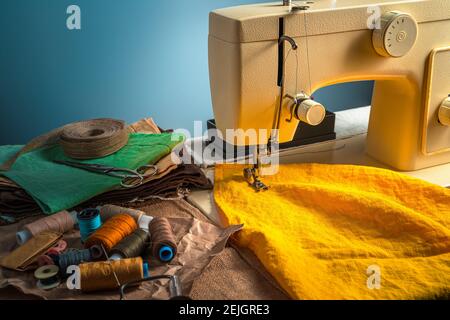 Colorful sewing background with sewing machine and accessories on blue background. Side view with copy space. Stock Photo