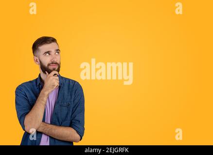 Dreamy hipster guy thinking over something, looking at empty space on orange studio background Stock Photo