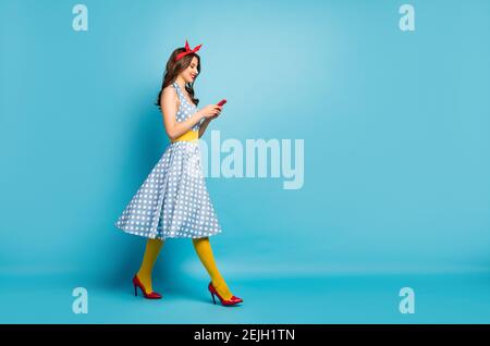 Full length body size profile side view of nice attractive lovely glamorous focused cheerful wavy-haired girl walking using cell, isolated on bright v Stock Photo
