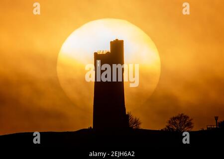 People stand on Castle Hill as the Sun sets over Victoria Tower, Castle Hill, Huddersfield. The tower was built to commemorate Queen Victoria's Diamond Jubilee of 1897 however the history of human activity on the Castle Hill dates back over 4000 years in Huddersfield, UK on 2/22/2021. (Photo by Mark Cosgrove/News Images/Sipa USA) Credit: Sipa USA/Alamy Live News Stock Photo