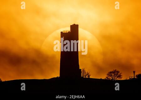 People stand on Castle Hill as the Sun sets over Victoria Tower, Castle Hill, Huddersfield. The tower was built to commemorate Queen Victoria's Diamond Jubilee of 1897 however the history of human activity on the Castle Hill dates back over 4000 years in Huddersfield, UK on 2/22/2021. (Photo by Mark Cosgrove/News Images/Sipa USA) Credit: Sipa USA/Alamy Live News Stock Photo