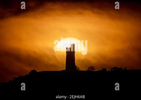 People stand on Castle Hill as the Sun sets over Victoria Tower, Castle Hill, Huddersfield. The tower was built to commemorate Queen Victoria's Diamond Jubilee of 1897 however the history of human activity on the Castle Hill dates back over 4000 years in Huddersfield, UK on 2/22/2021. (Photo by Mark Cosgrove/News Images/Sipa USA) Credit: Sipa USA/Alamy Live News Stock Photo