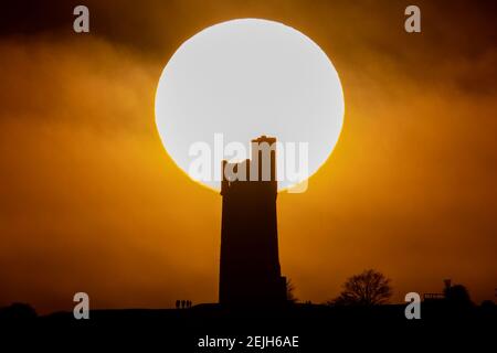 People stand on Castle Hill as the Sun sets over Victoria Tower, Castle Hill, Huddersfield. The tower was built to commemorate Queen Victoria's Diamond Jubilee of 1897 however the history of human activity on the Castle Hill dates back over 4000 years in Huddersfield, UK on 2/22/2021. (Photo by Mark Cosgrove/News Images/Sipa USA) Credit: Sipa USA/Alamy Live News Stock Photo