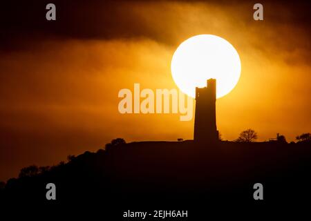 People stand on Castle Hill as the Sun sets over Victoria Tower, Castle Hill, Huddersfield. The tower was built to commemorate Queen Victoria's Diamond Jubilee of 1897 however the history of human activity on the Castle Hill dates back over 4000 years in Huddersfield, UK on 2/22/2021. (Photo by Mark Cosgrove/News Images/Sipa USA) Credit: Sipa USA/Alamy Live News Stock Photo