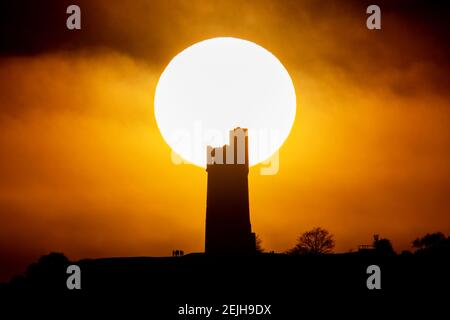 People stand on Castle Hill as the Sun sets over Victoria Tower, Castle Hill, Huddersfield. The tower was built to commemorate Queen Victoria's Diamond Jubilee of 1897 however the history of human activity on the Castle Hill dates back over 4000 years in Huddersfield, UK on 2/22/2021. (Photo by Mark Cosgrove/News Images/Sipa USA) Credit: Sipa USA/Alamy Live News Stock Photo