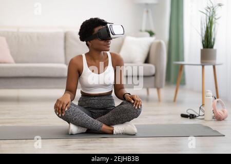 Black Lady Wearing Virtual Reality Headset Doing Yoga At Home Stock Photo