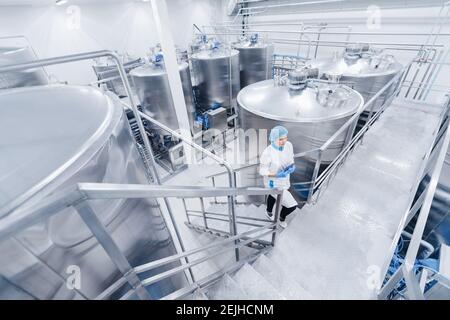 Female worker operator in uniform holding computer tablet near food factory production line. Stock Photo