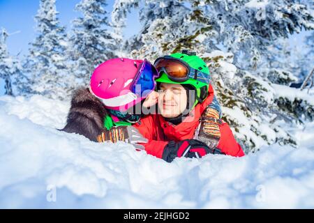Snowboarder man and woman skier hugging and having fun on background of winter forest and snow. Sunlight in mountains. Stock Photo