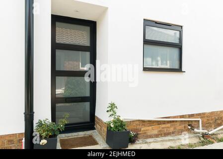 A modern typical house which has been renovated with white render and dark grey UPVc plastic double glazed windows and doors. Stock Photo