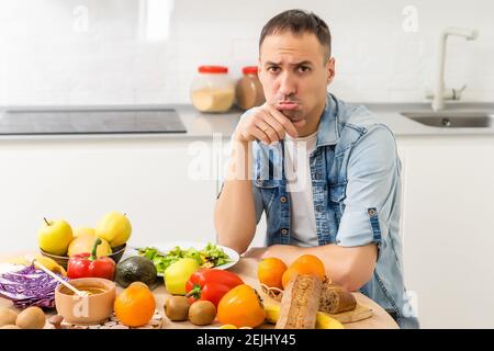 Happy young man preparing romantic dinner searching vegetable recipes diet menu, smiling husband cooking healthy vegan food cut salad in kitchen Stock Photo