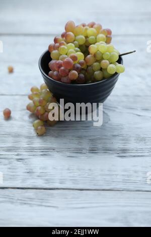 Red green grapes in a black bowl on a gray wooden table and copy space. Stock Photo