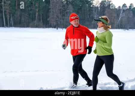 Smiling senior couple jogging in snowy winter park.