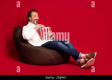 Full body profile photo of excited impressed guy hold pop corn box look empty space isolated on dark red color background. Stock Photo