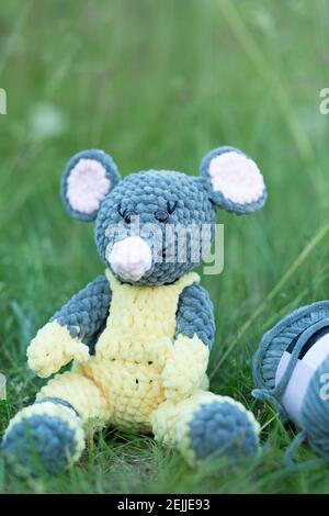 Handmade knitted toy. Knitted mouse in yellow overalls on the grass with place for your text Stock Photo