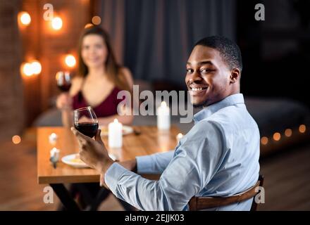 Portraif Of Happy Interracial Couple Sitting At Table In Restaurant, Drinking Wine Stock Photo