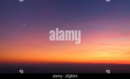 Evening colorful purple-pink sky with red clouds and orange horizon, crescent moon. Aerial photography, sky over the whole photo. Stock Photo