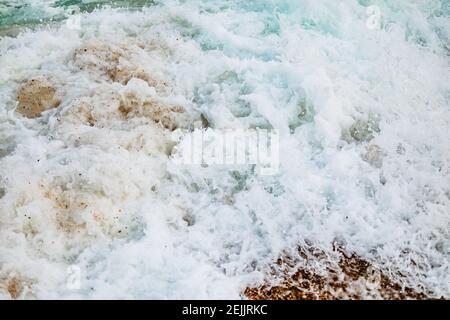 A storm of large foamy, seething, sea waves close-up mixed with sand. Stone coast with a big wave. The sweetness of the sea mixed with the hardness of Stock Photo
