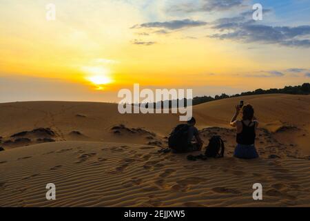 A couple watching a colorful sunset on la dune du Pyla, France Stock Photo