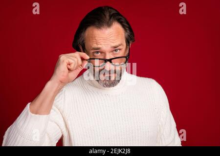 Photo portrait of serious old man wearing glasses white warm knitted sweater isolated on red color background. Stock Photo