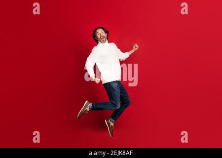 Full size profile portrait of astonished guy jumping open mouth celebrate isolated on red color background. Stock Photo