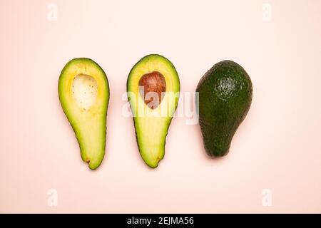 Halved and whole avocados on pink table Stock Photo