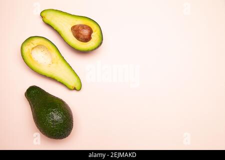 Halved and whole avocados on pink table Stock Photo