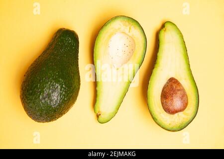 Halved and whole avocados on yellow table Stock Photo