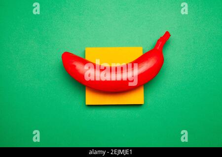 Bright composition of red banana and yellow sticky notes on green surface Stock Photo