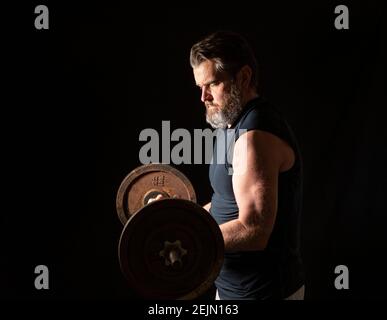 Strong, active, middle aged man with gray beard lifting heavy weights in studio setting. Stock Photo