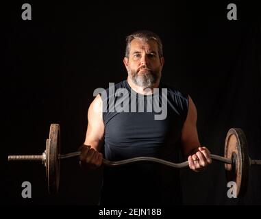 Strong, active, middle aged man with gray beard lifting heavy weights in studio setting. Stock Photo