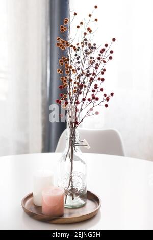 A bouquet of red elegant dry flowers potted in a bottle next to a couple of aromatic candles. Stock Photo