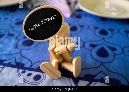 wooden dummy sitting on a restaurant table holding a welcome sign, selective focus on the text, horizontal Stock Photo