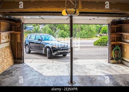 Black Suv turning into garage with automatic overhead door opener - grainy unfinished surfaces and pavement - Suburban neighborhood with trees Stock Photo