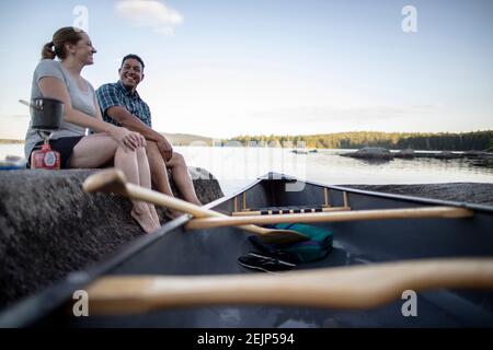 African american man and white woman sit on rock on lake with canoe Stock Photo