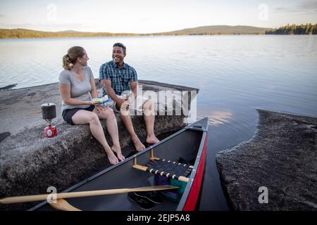 Couple cook meal and laugh while taking break from canoe trip, Maine Stock Photo